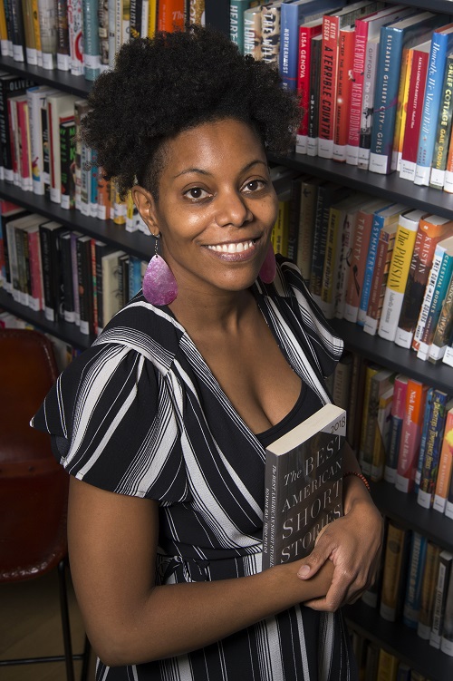 the author standing in front of a bookshelf holding a book, photo by Wesley Bunnell